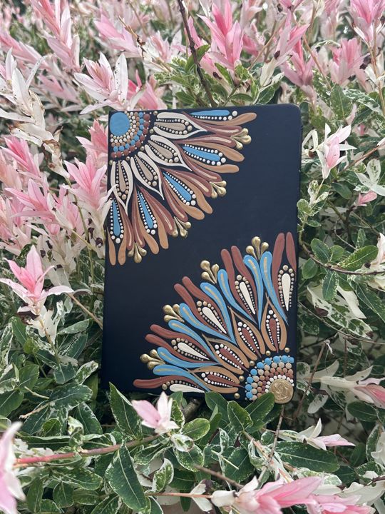 Notitieboek met halve mandala's in blauw, roest en crème tussen roze bladeren